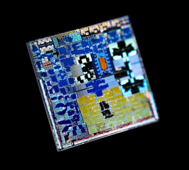 A die shot of the Apple M1 chip under coloured light: blocks of CPU, GPU and cache in blue and yellow on black